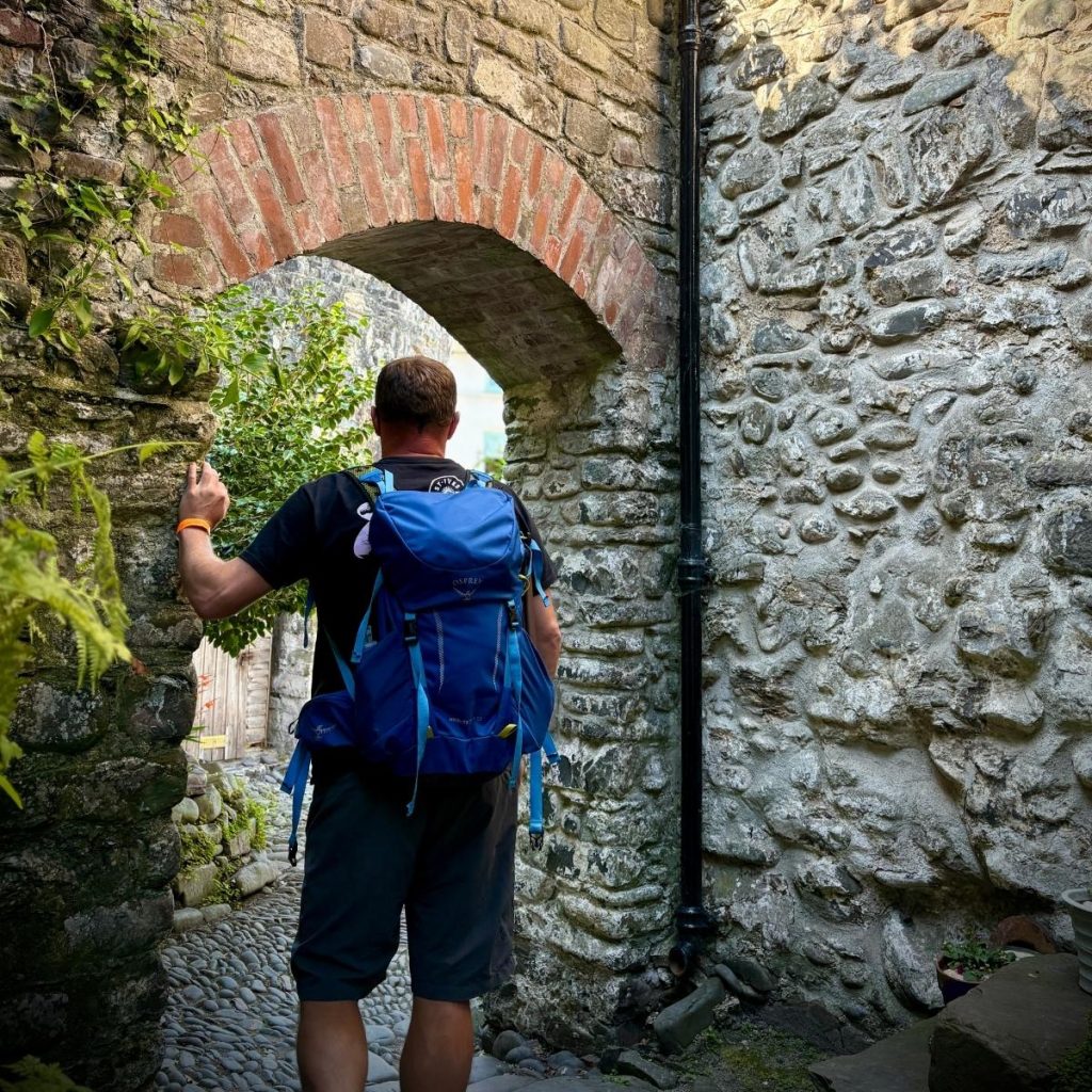 Man standing in an arch way of an alleyway with rucksack on mid walk through the arch