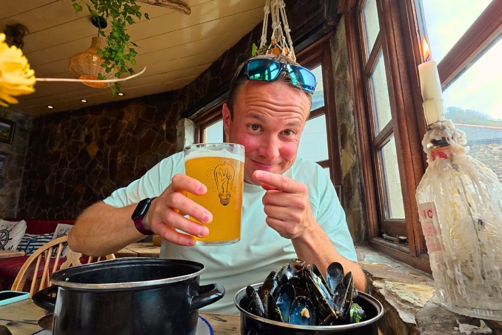 Man holding a pint of local craft beer inside The Rashleigh Inn in Polkerris with mussels on the table. 