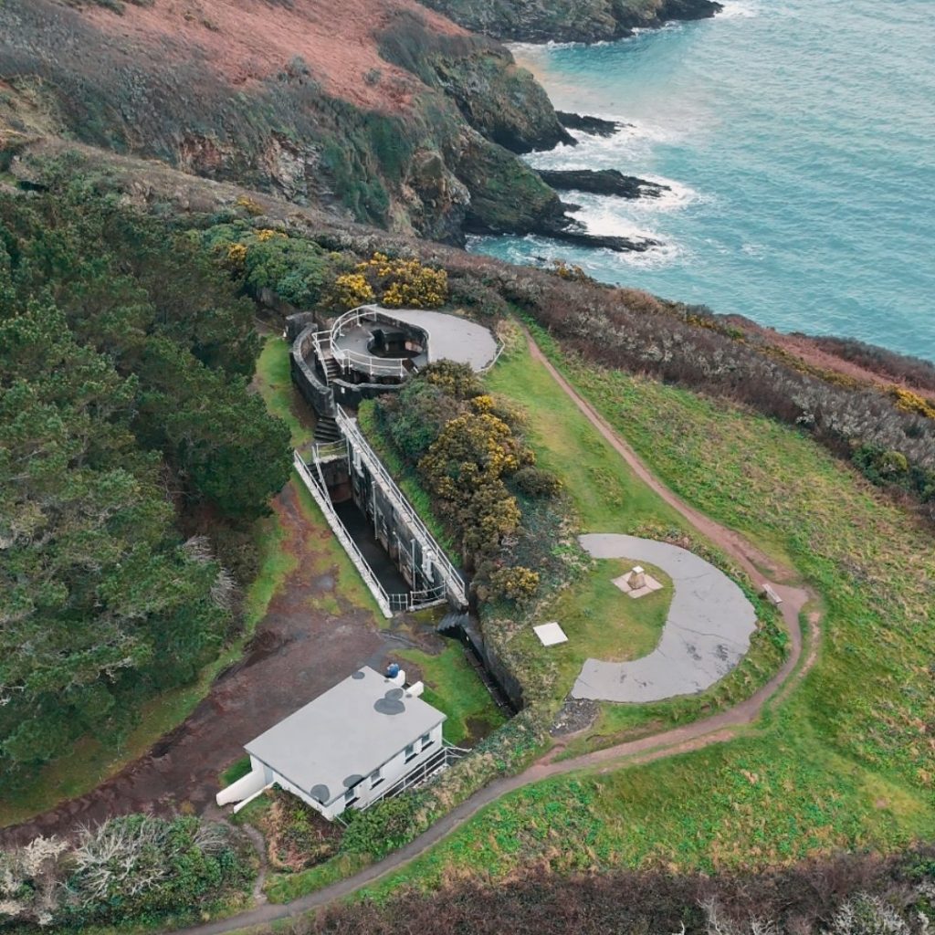 Aerial view of a coastal wartime defence structure overlooking the sea, with concrete gun emplacements and surrounding cliffs. This is the gun placements at St Anthony's Head, Cornwall.