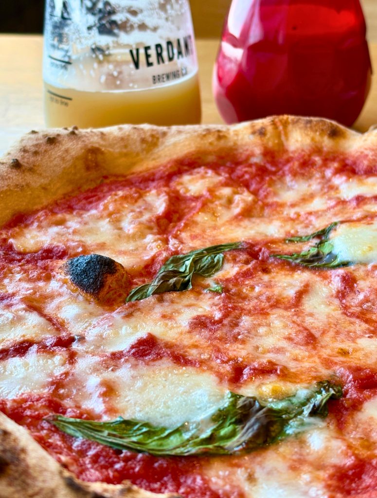 Wood fired margherita pizza with melted cheese and basil served with a hazy Verdant craft beer at Schooners in St Agnes overlooking Trevaunance Cove.