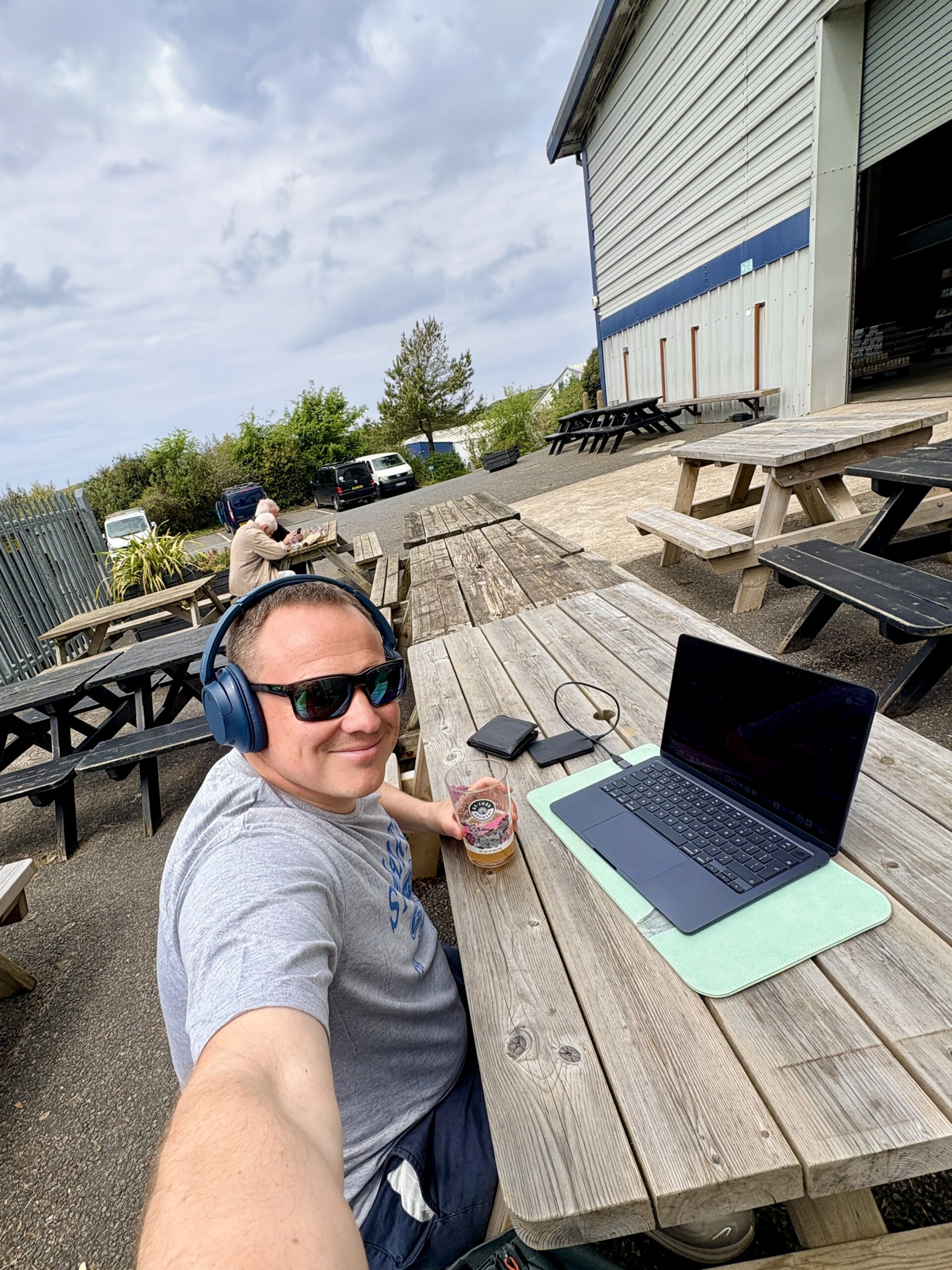 Dan Working on his Mac at St Ives Brewery in the sunshine with a pint in hand smiling
