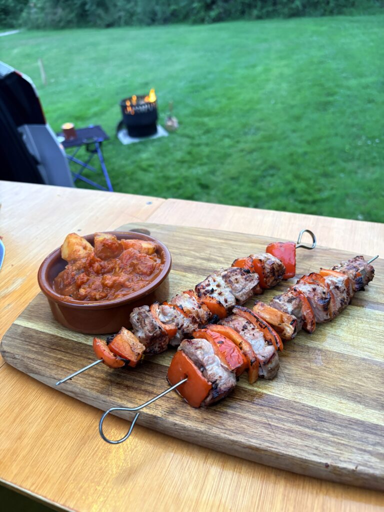 Field to Fork camp cooking featuring smoky pork kebabs and homemade patatas bravas cooked outdoors at a campsite in Cornwall over an open flame.
