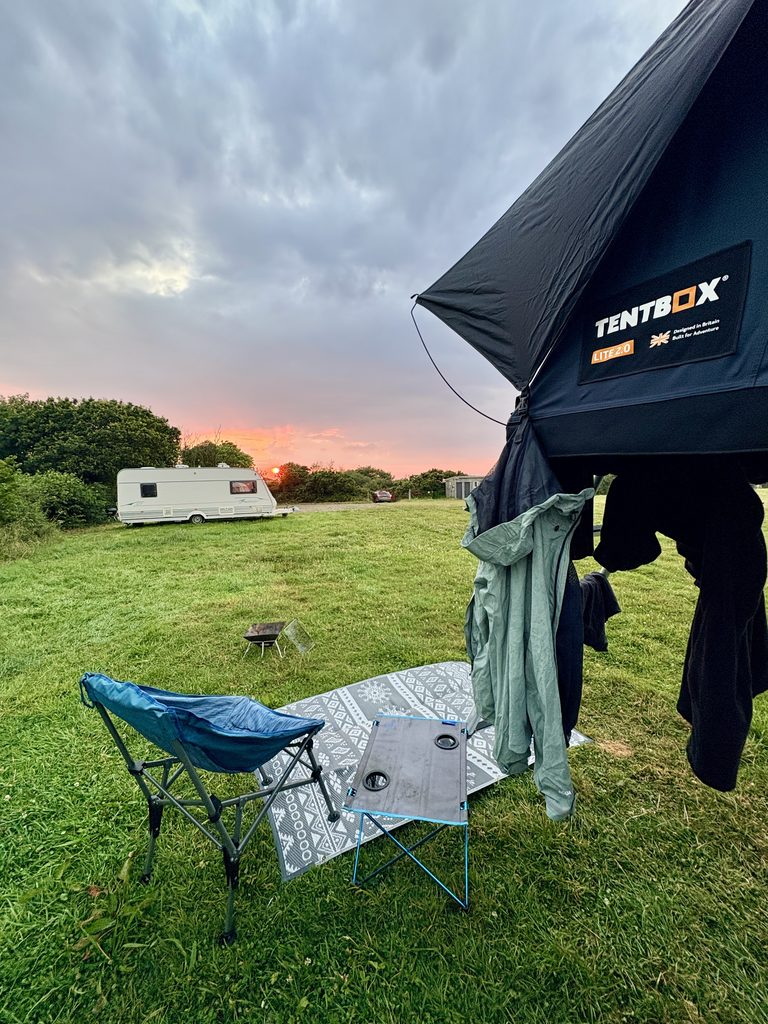 TentBox camping setup at Crackington Haven Campsite with a dramatic sunset sky, grassy field and caravan in the background.